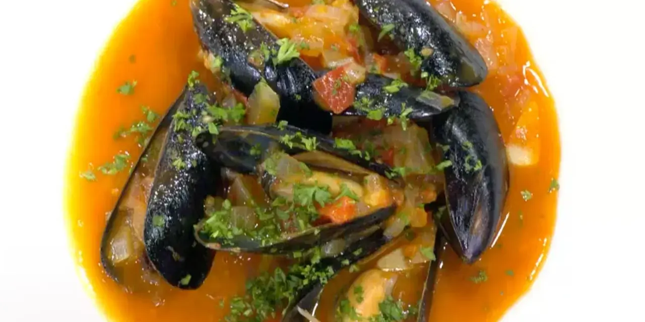 Mejillones a la marinera, jugosos y frescos, nadan en una salsa roja vibrante con perejil picado.