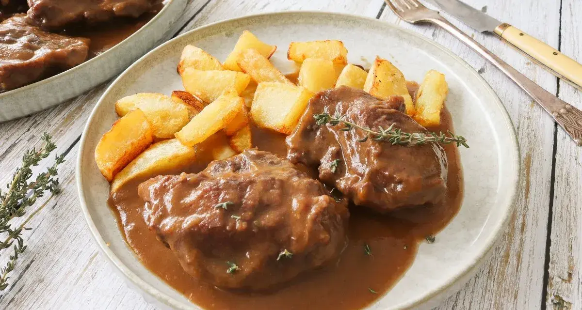Dos tiernas porciones de pata de ternera guisada en su jugo, acompañadas de patatas rústicas fritas y una ramita de tomillo.