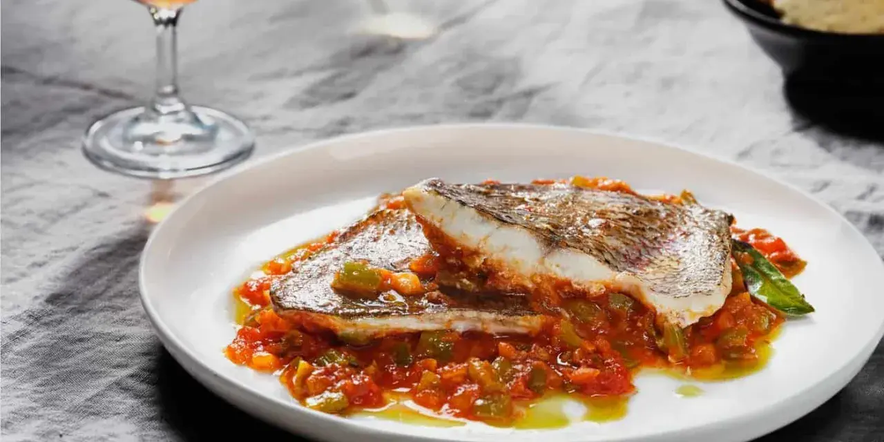 Deliciosa urta a la roteña servida en plato blanco, con vino y pan tostado al fondo.
