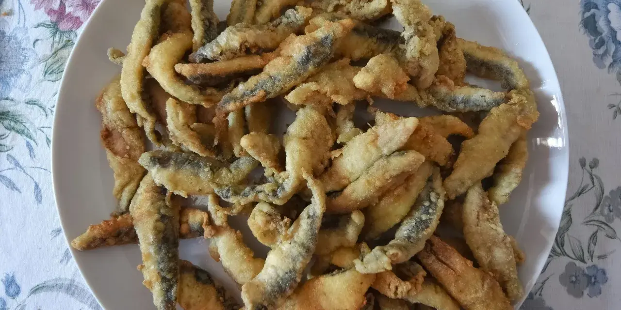 Un plato blanco lleno de boquerones fritos crujientes, listos para disfrutar.