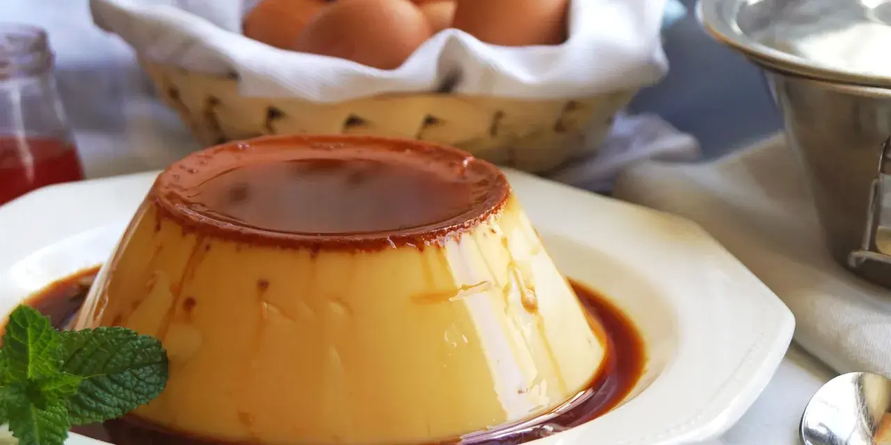 Delicioso flan de huevo casero con caramelo líquido, decorado con menta. En el fondo, una cesta con huevos frescos.