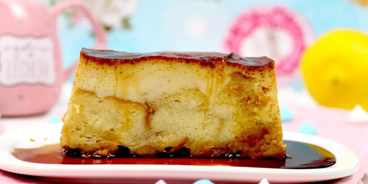 Un trozo de pan de calatrava con caramelo líquido, sobre un plato blanco, con merengues de colores y un limón al fondo.