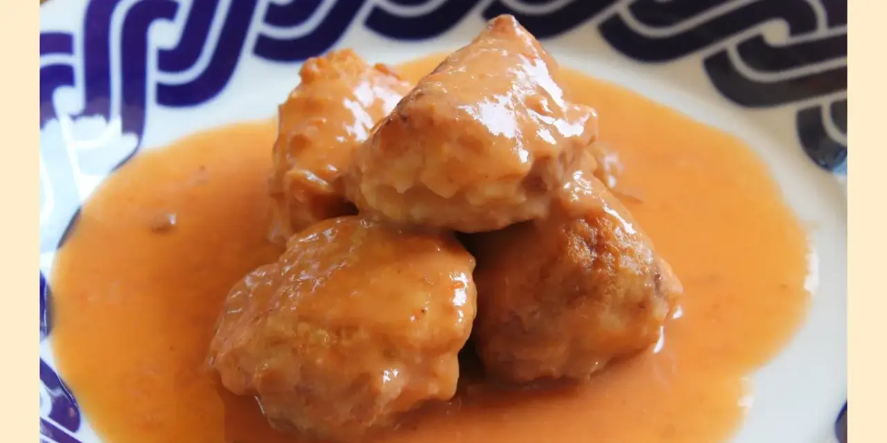 Deliciosas albóndigas de rape en una cremosa salsa naranja, servidas en un plato con borde azul.