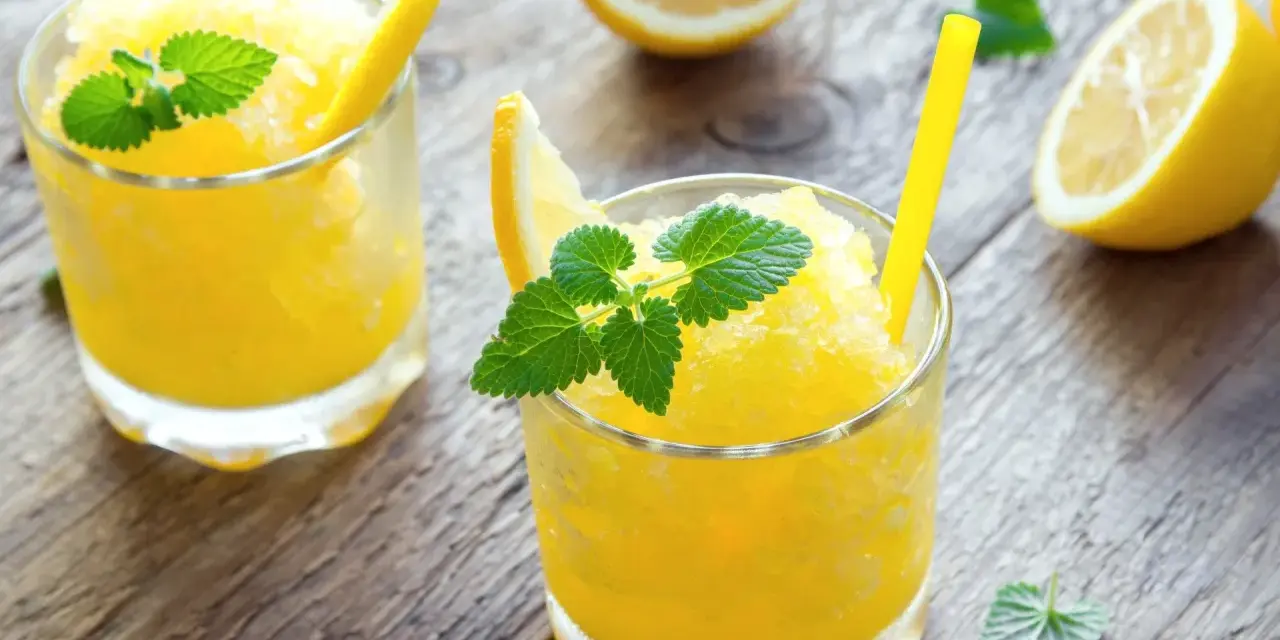 Refrescante granizado de limón, perfecto para un día caluroso. Servido en vasos con rodajas de limón y hojas de menta.