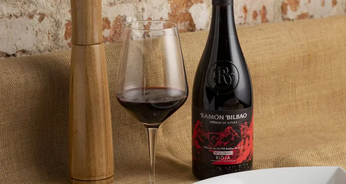 Una copa de vino seco, una botella de Ramón Bilbao Rioja y un plato de atún sellado, listos para una cena.