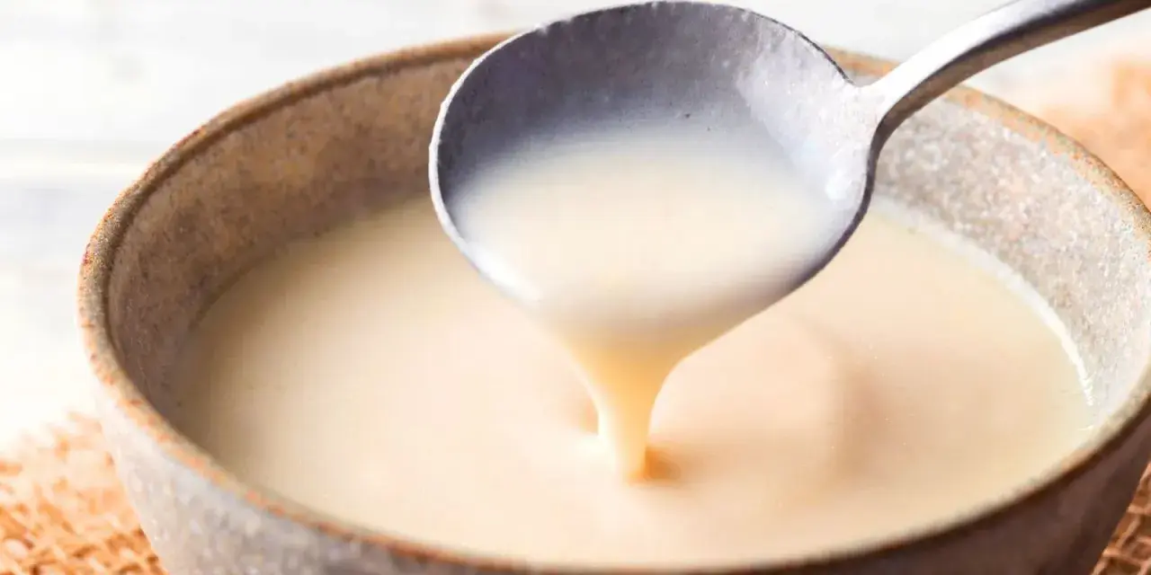 Cuchara sirviendo crema inglesa cremosa en un cuenco rústico.