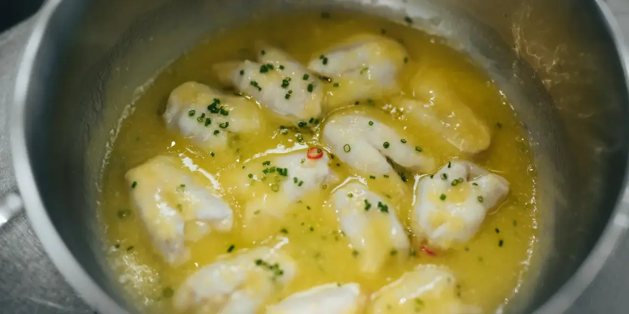 Trozo de bacalao al pil pil burbujeando en una sartén con aceite de oliva, ajo y perejil picado.