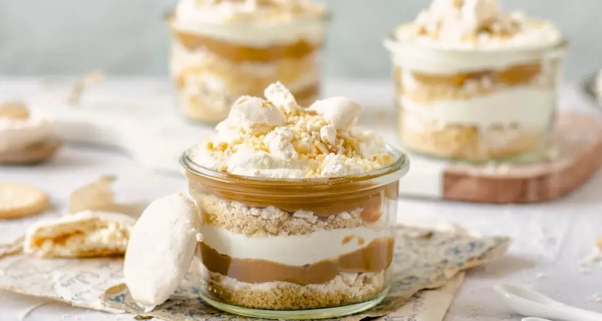 Postres en vaso con capas de bizcocho, crema y dulce de leche, coronados con merengue y polvito canario.