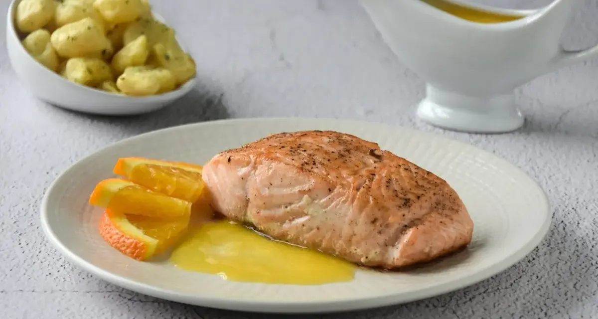 Filete de salmón a la naranja, servido con gajos de naranja y una salsa dorada. Acompañado de gnocchis en un cuenco.