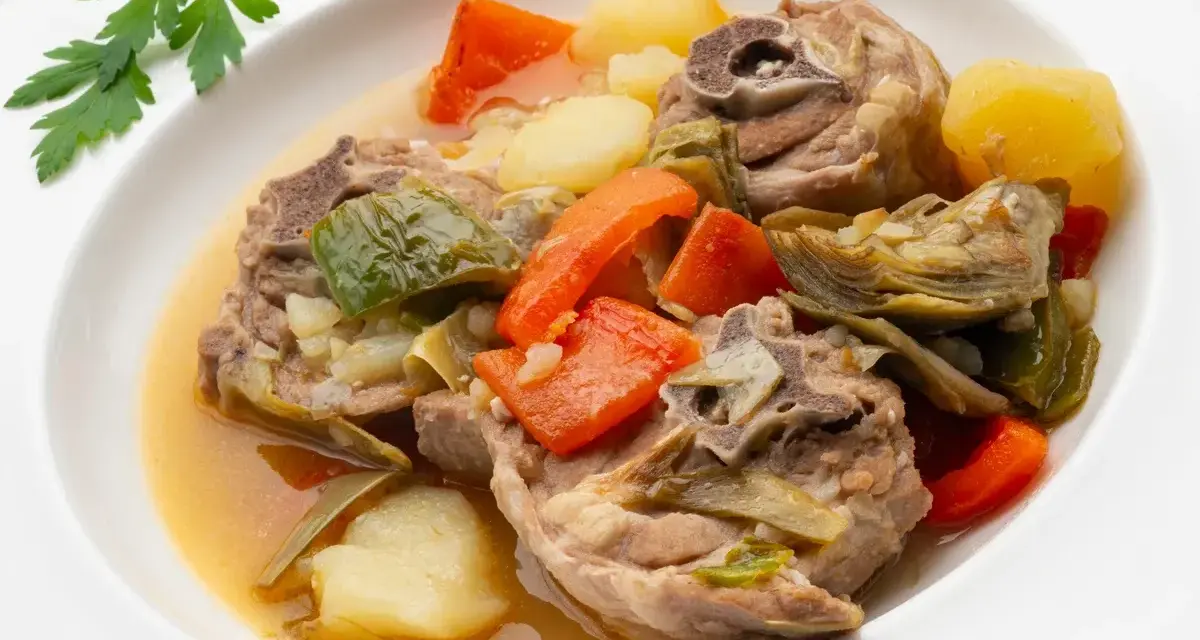 Cordero guisado receta tradicional con patatas, zanahorias y alcachofas en un plato blanco.