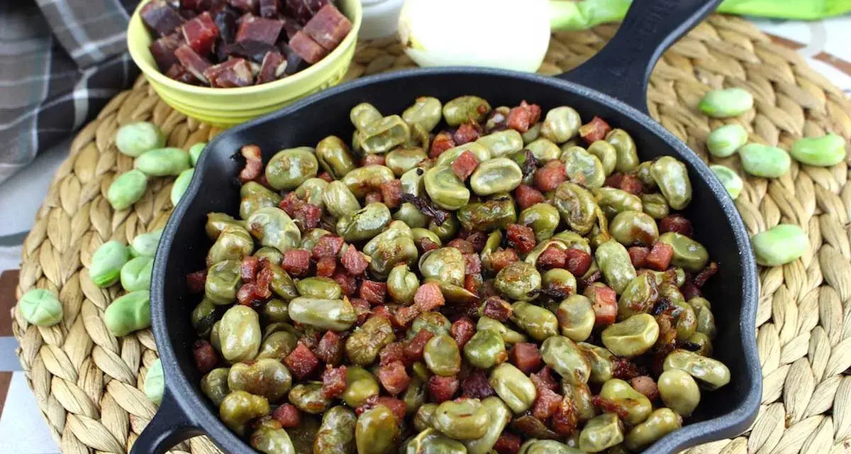 Habas tiernas salteadas con trocitos de jamón en una sartén de hierro fundido, un plato tradicional y delicioso.