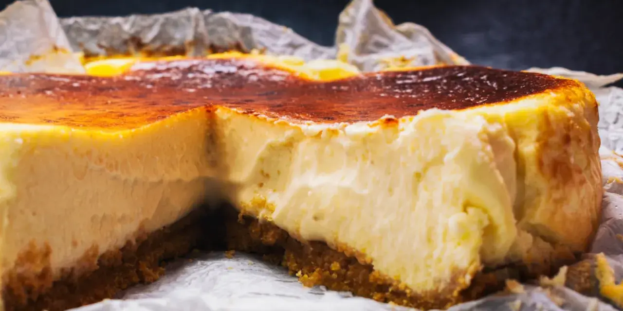 Tarta de queso cremosa con base crujiente y cobertura dorada, recién salida del horno.