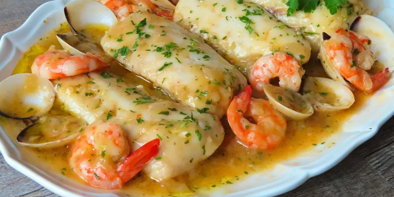 Merluza a la marinera con gambas y almejas, todo bañado en una deliciosa salsa dorada y espolvoreado con perejil fresco.
