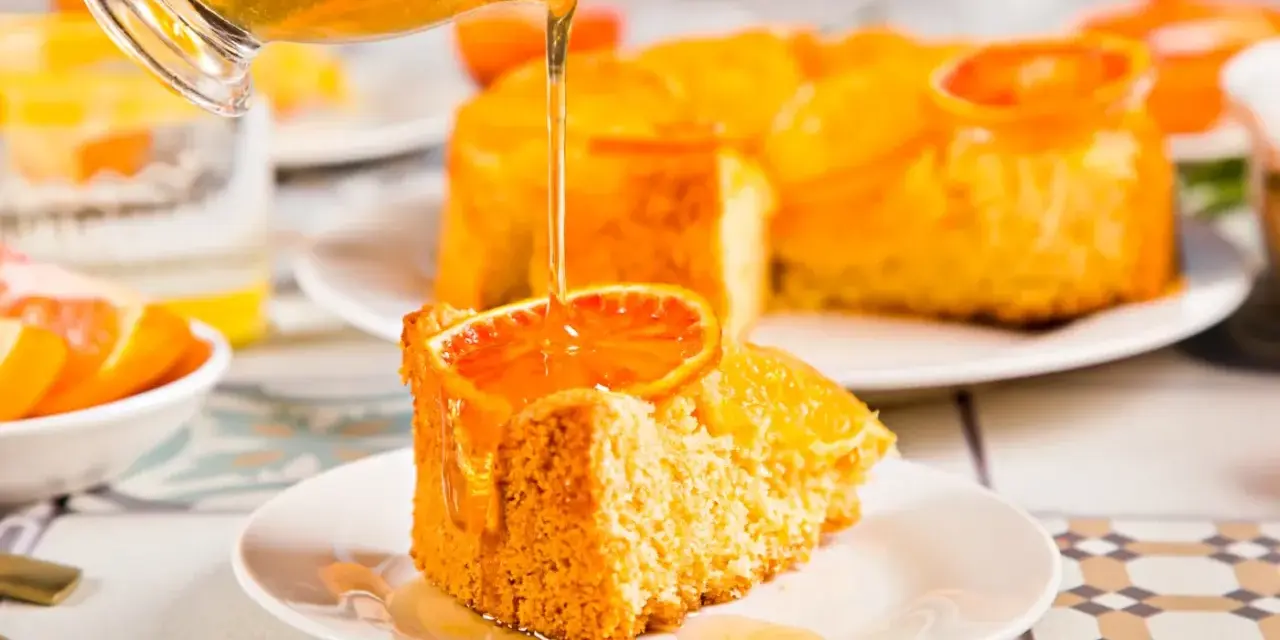 Un trozo de tarta de naranja esponjosa, decorado con una rodaja de naranja y bañado en un almíbar dorado.