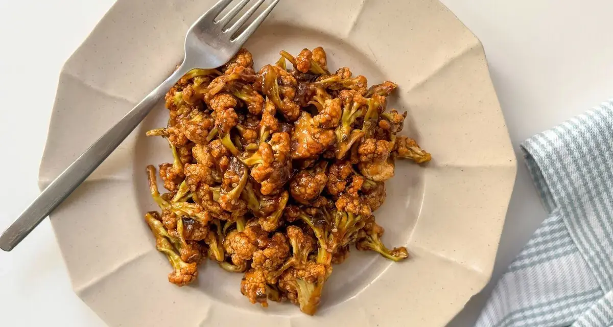 Coliflor glaseada, una de las mejores recetas con coliflor. Servida en plato beige con tenedor plateado y servilleta a cuadros.