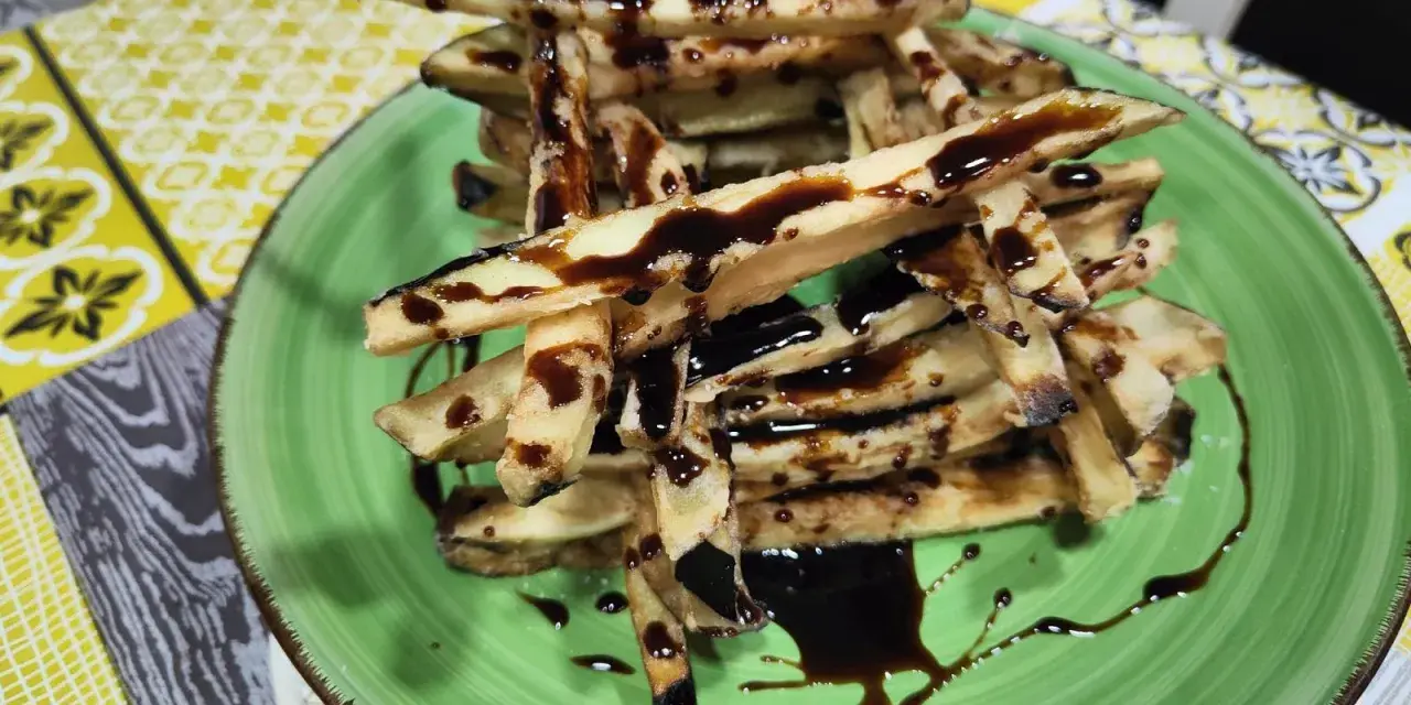 Berenjenas fritas en forma de bastones, bañadas en miel oscura, servidas en un plato verde.