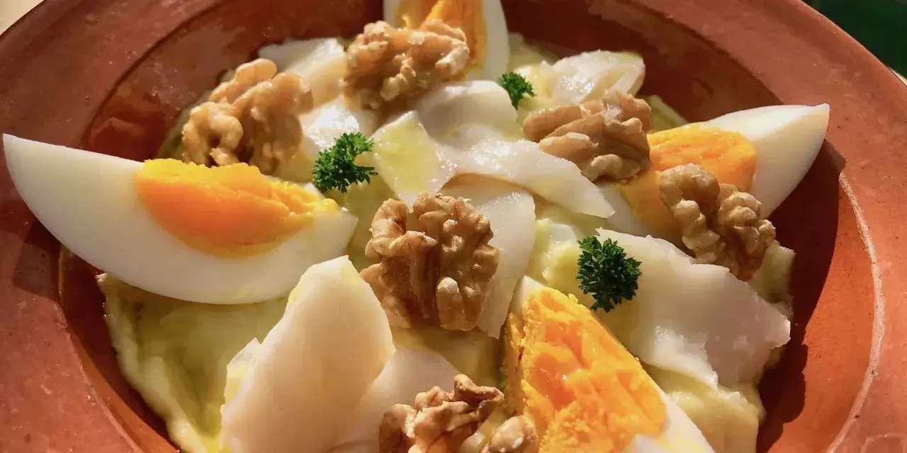 Delicioso plato de atascaburras receta con huevo duro, nueces y perejil en una cazuela de barro.