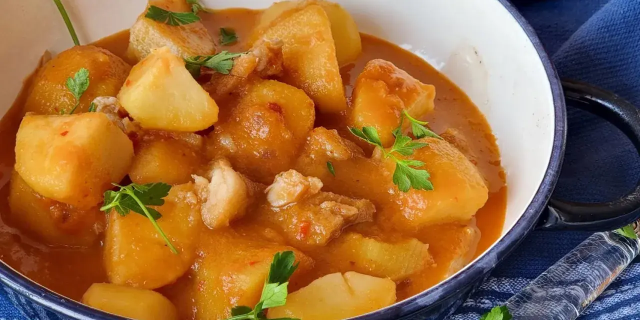 Un reconfortante plato de patatas con bacalao en una salsa rojiza, adornado con perejil fresco.