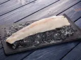 Filete de pescado rosado fresco sobre hielo picado en una tabla negra, listo para cocinar.