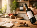 Mano sostiene botella de vino tinto, tres copas llenas y un libro abierto. ¿Que vino es mejor?