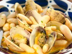 Un plato humeante de fabes con almejas, con judías blancas tiernas y almejas jugosas en una salsa dorada, adornado con perejil picado.
