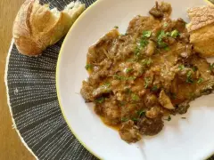 Fricandó, hecho con la parte de la ternera llamada "espalda", servido en plato blanco con pan.