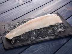Filete de pescado rosado fresco sobre hielo picado en una tabla negra, listo para cocinar.