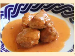 Deliciosas albóndigas de rape en una cremosa salsa naranja, servidas en un plato con borde azul.
