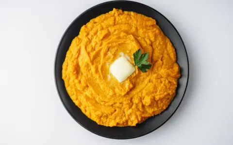 Un cremoso puré de boniato, coronado con una pastilla de mantequilla y una ramita de perejil, listo para disfrutar.