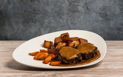Delicioso plato de cola de toro en salsa, acompañado de patatas rústicas y zanahorias glaseadas.