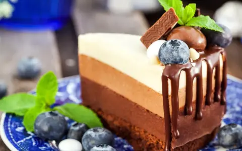 Deliciosa tarta de tres chocolates, con capas de chocolate blanco, con leche y negro, decorada con arándanos y menta.