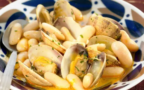 Un plato humeante de fabes con almejas, con judías blancas tiernas y almejas jugosas en una salsa dorada, adornado con perejil picado.