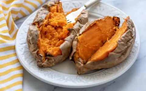 Dos mitades de boniato asado en freidora de aire, servidas en un plato blanco con un tenedor.