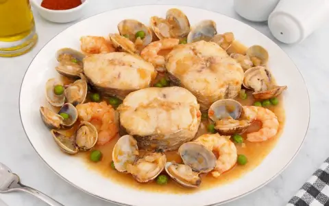 Merluza a la cazuela con gambas, almejas y guisantes en una salsa sabrosa.