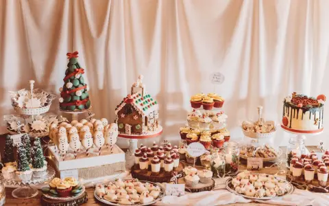 Mesa llena de postres navideños: casa de jengibre, árbol de macarons, muñecos de nieve, cupcakes y galletas.