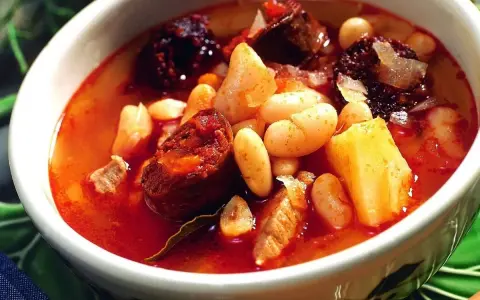 Un reconfortante plato de alubias con chorizo, trozos de morcilla y patatas en un cuenco blanco.