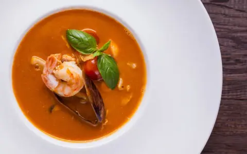 Un plato de zarzuela de pescado con gambas, mejillones y tomate, decorado con albahaca fresca.