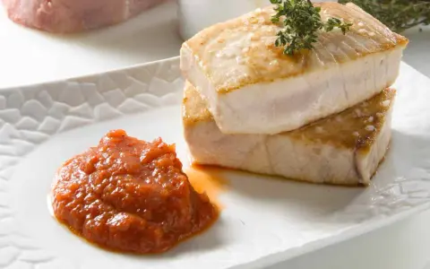 Dos trozos de atún a la plancha apilados, con una cucharada de salsa de tomate y una ramita de tomillo.