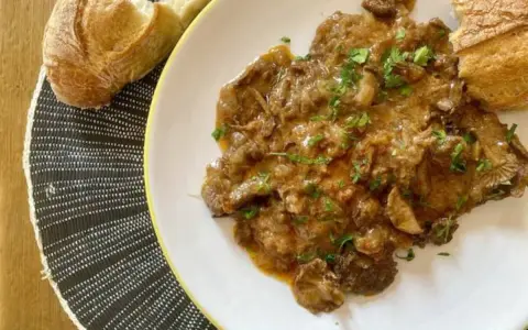 Fricandó, hecho con la parte de la ternera llamada "espalda", servido en plato blanco con pan.