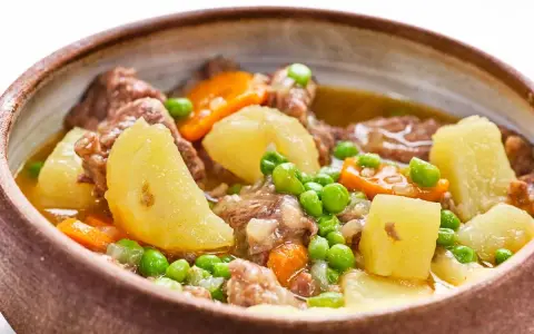 Un reconfortante ragú con trozos de carne tierna, patatas, zanahorias y guisantes en un cuenco rústico.