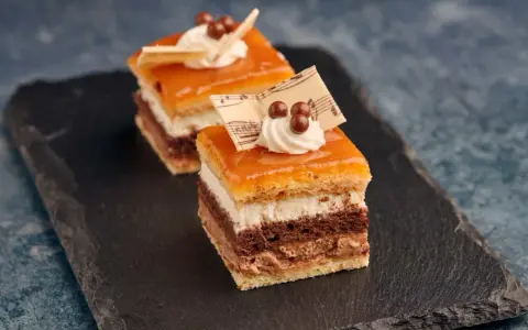 Deliciosa tarta San Marcos en porciones, con capas de bizcocho, crema y cobertura anaranjada, decorada con nata y notas musicales de chocolate.