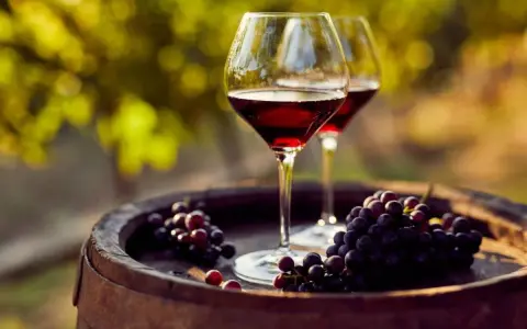 Dos copas de vino tinto y uvas sobre un barril de madera, evocando la esencia de la cosecha Ribera del Duero.