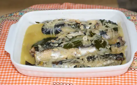 Caballa en escabeche servida en una fuente blanca, con cebolla, laurel y un líquido dorado.