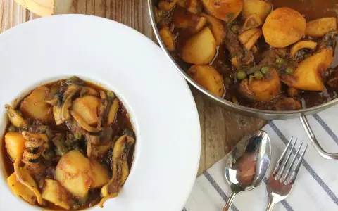 Un plato de papas con choco, un guiso casero con trozos de patata, guisantes y calamares en una rica salsa.