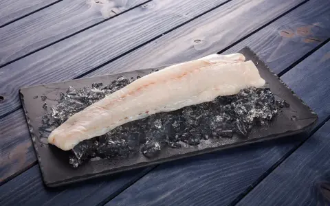 Filete de pescado rosado fresco sobre hielo picado en una tabla negra, listo para cocinar.