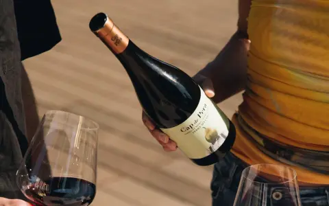 Manos sirven vino tinto de una botella Cap de Pera. Opiniones sobre "llàgrimes de tardor" y la experiencia.