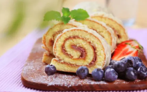 Brazo de gitano en rodajas con fresas y arándanos sobre tabla de madera.