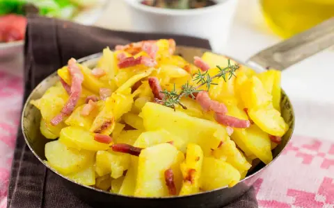 Patatas al microondas con trocitos de bacon crujiente y romero fresco, servidas en una sartén metálica. ¡Un plato sencillo y delicioso!
