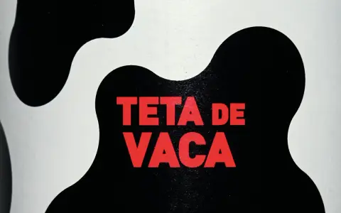 Texto rojo "TETA DE VACA" sobre un fondo blanco y negro con manchas de vaca.