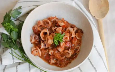 Deliciosos chipirones en salsa de tomate, servidos en un cuenco de cerámica, decorados con perejil fresco.